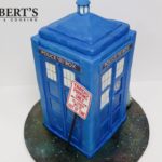 Dr Who Tardis Cake | The TARDIS is Homemade fondant on an “orange velvet” cake filled and covered in dark chocolate orange ganache. The board is covered in white fondant then baked for 10 minutes at 80C to set it hard before it was airbrushed with food colour to look like a galaxy. The signage is icing sheets printed with edible ink. I made the Dalek from homemade modelling chocolate. | https://robertscakesandcooking.com/tardis-cake-and-construction-photos/